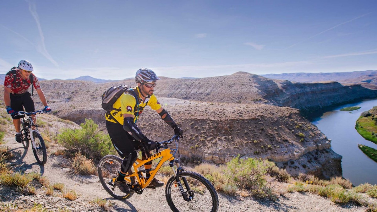 Two mountain bikers on a ridge trail above a river canyon